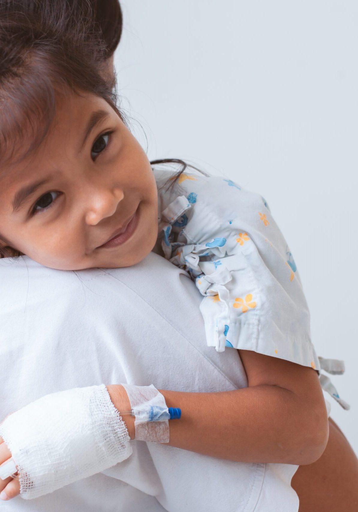 Sick asian child girl who have IV solution bandaged smiling and  hugging her mother with love in the hospital